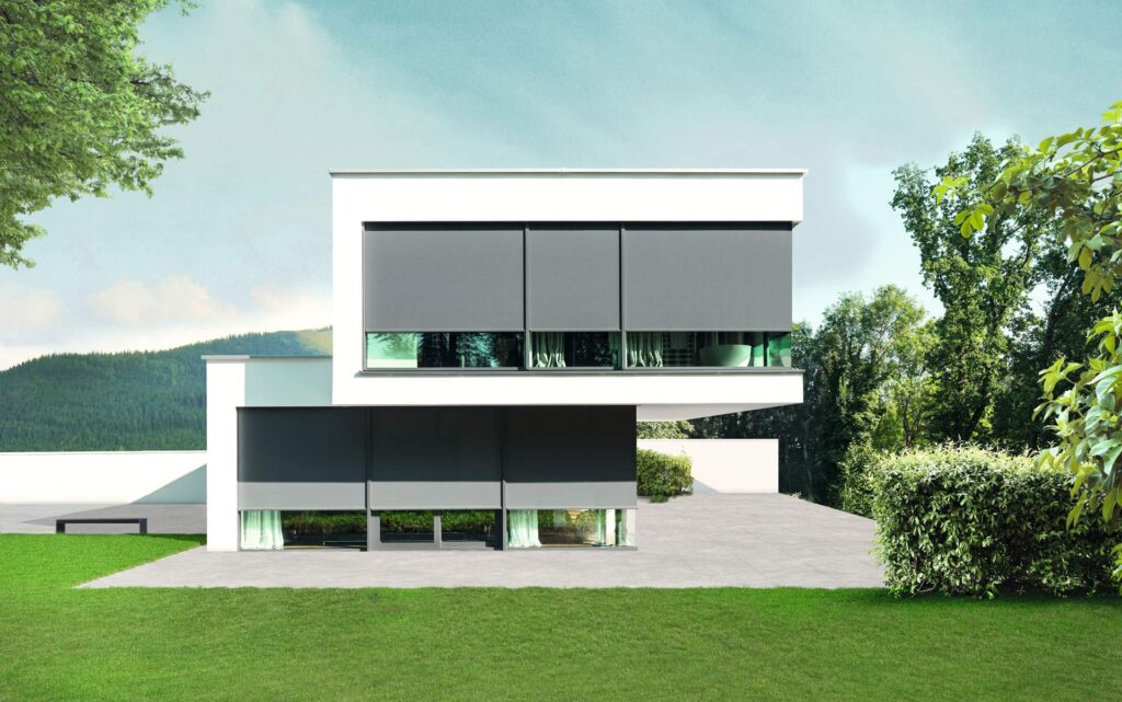 Modernes weißes Haus mit großen Fenstern und grauen Außenjalousien umgeben von Grün