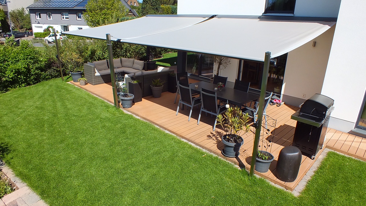 Eine moderne Terrasse mit Holzboden, schwarzem Grill, Gartenmöbeln und sonnigem Markisendach
